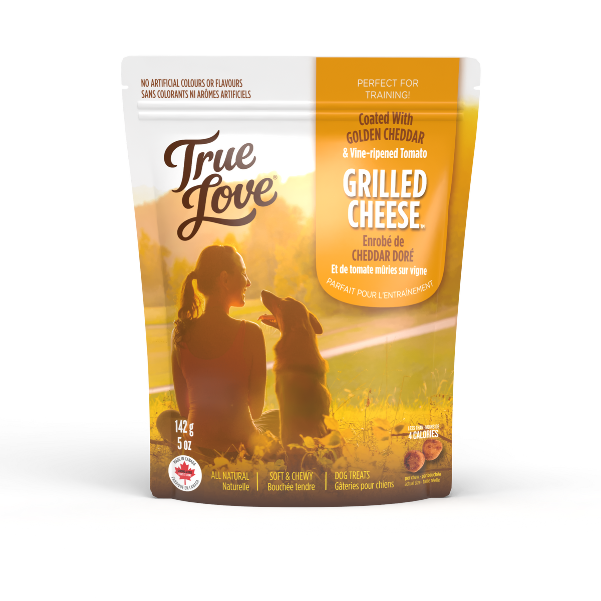 Bag of True Love dog treats with a woman smiling at her dog on the grass. Grilled Cheese flavour - golden cheddar and vine-ripened tomato.